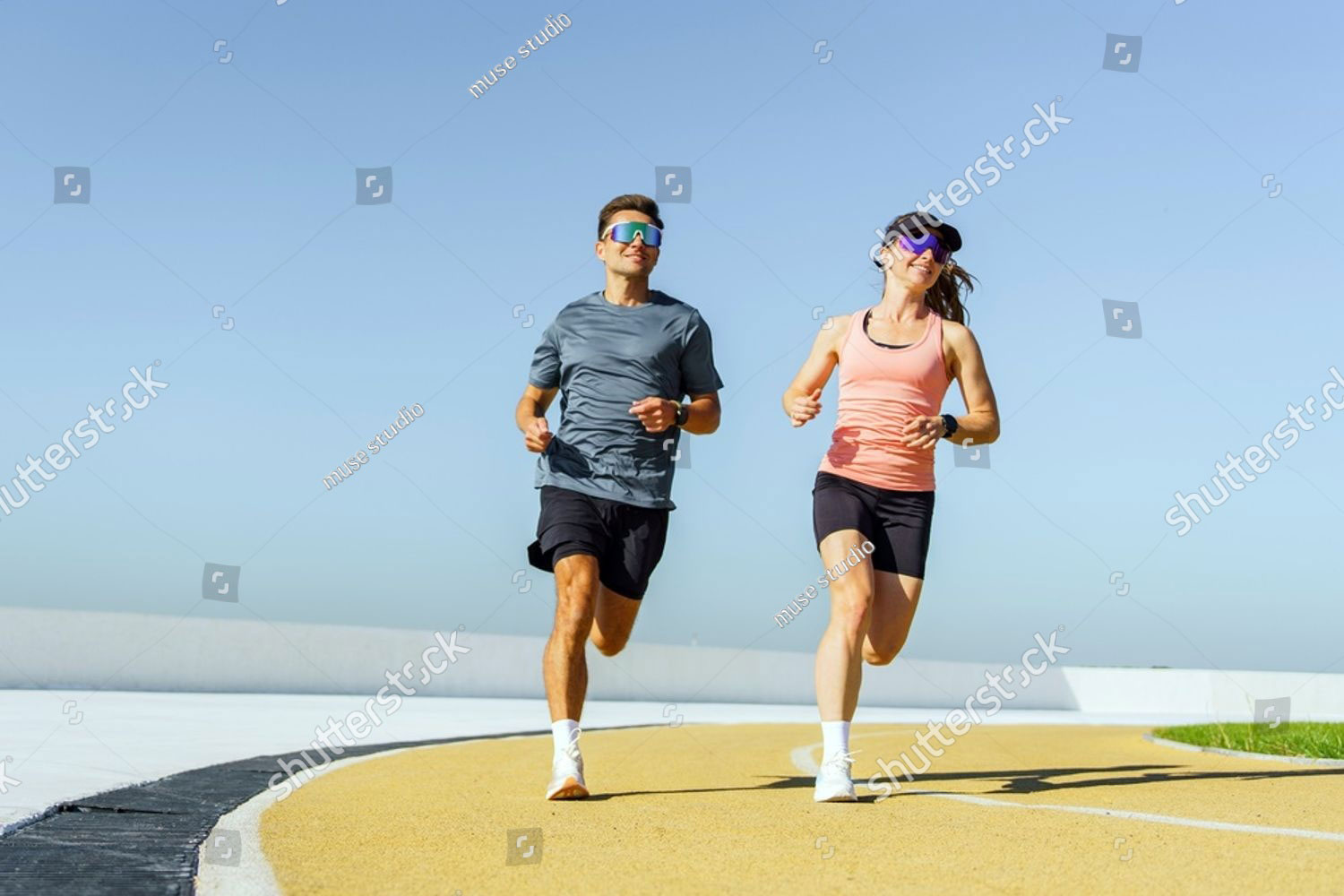 couple runs together on a sunny day at an outdoor track in a city